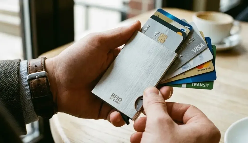 Primer plano de las manos de un hombre usando una cartera inteligente metálica con sistema de bloqueo RFID y tarjetas saliendo en abanico